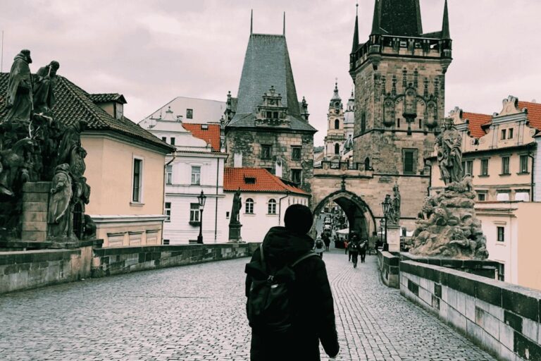 Person walking across Charles Bridge in Prague toward Old Town Bridge Tower on a cloudy day