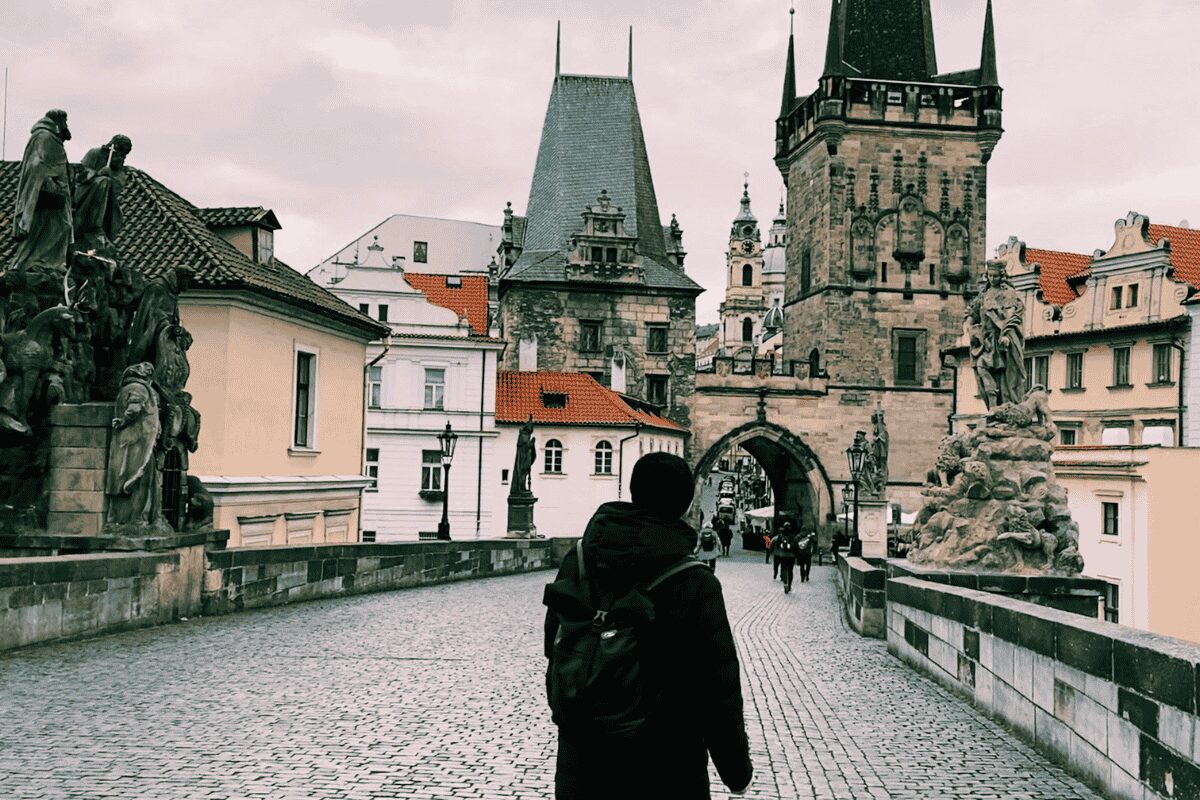 Person walking across Charles Bridge in Prague toward Old Town Bridge Tower on a cloudy day