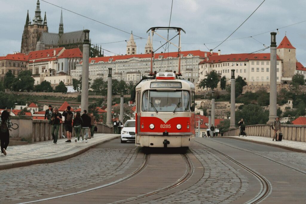 Prague tram crossing a cobblestone bridge with Prague Castle in the background