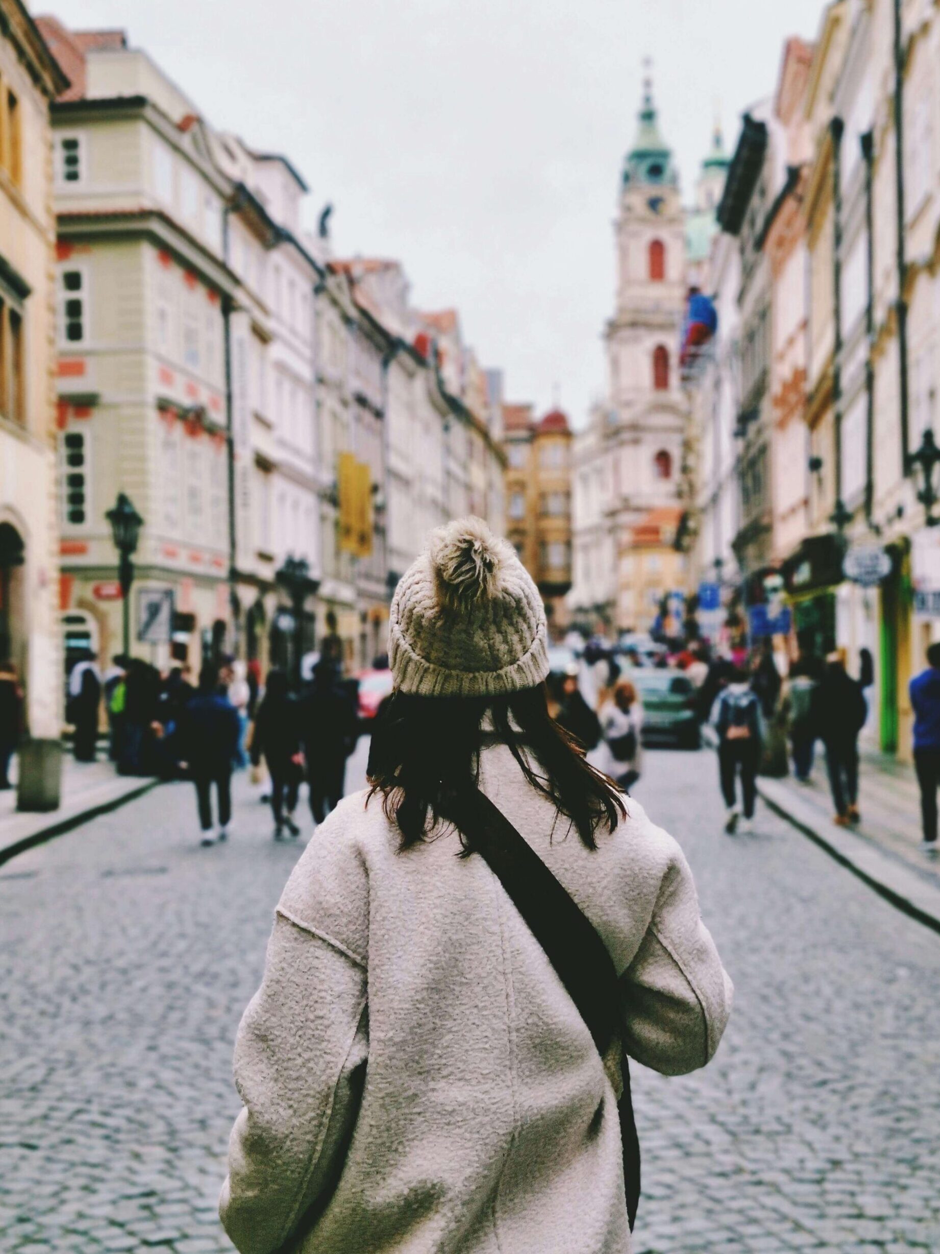 Woman exploring Prague Old Town cobblestone street with colorful historic buildings and church tower