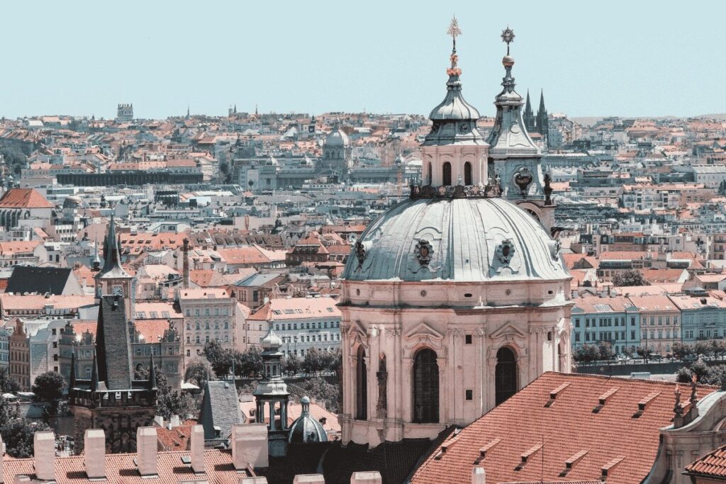 Aerial view of Prague's historic skyline featuring red rooftops and baroque church domes