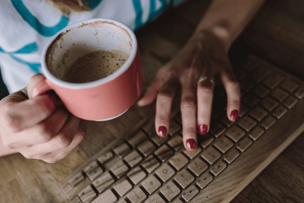 Woman typing on keyboard with coffee in hand 