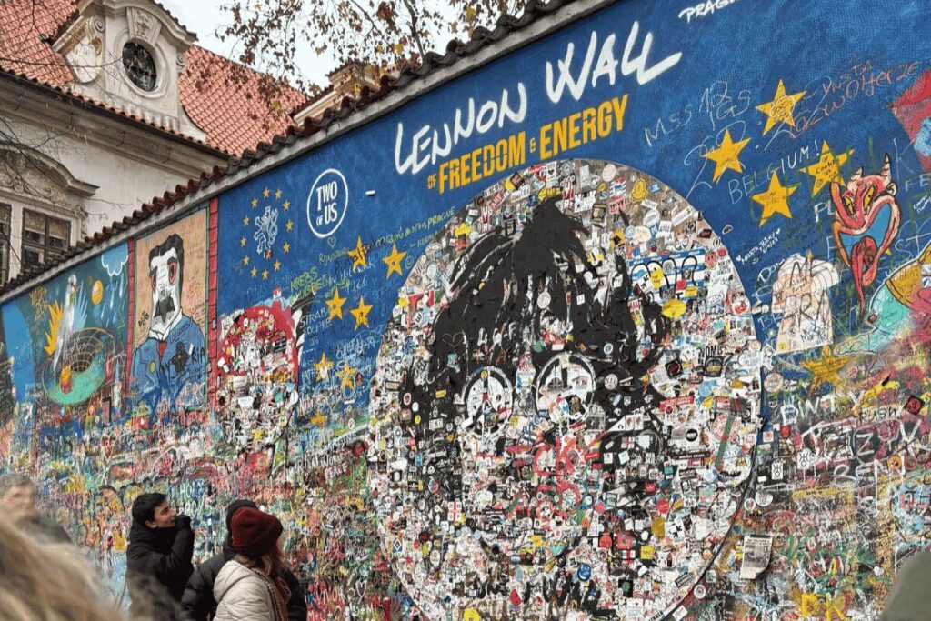 Visitors looking at colorful street art and messages on the John Lennon Wall in Prague