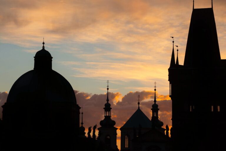 Silhouetted domes and towers of Prague’s Old Town skyline at sunset.