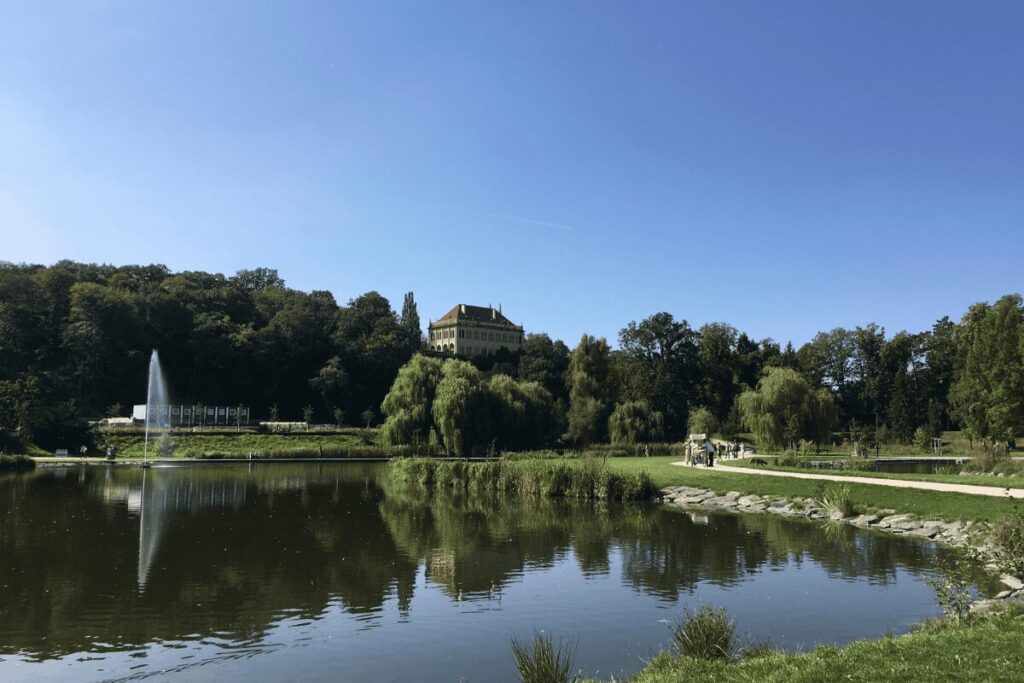 Pond and fountain in Stromovka park with tree-lined paths and greenery in Prague.