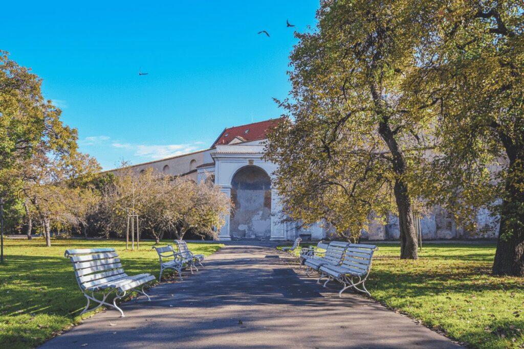 Benches and walking path in Vojanovy Gardens with the historic monastery buildings in the background in Prague.