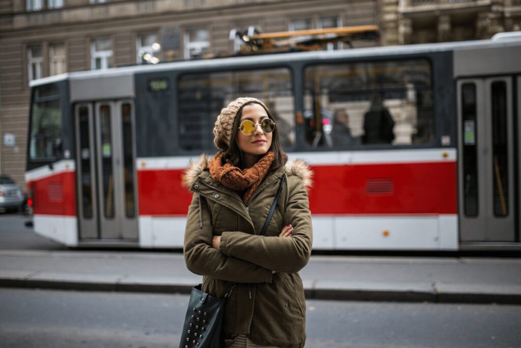 Woman standing confidently in front of a red Prague tram in winter clothing