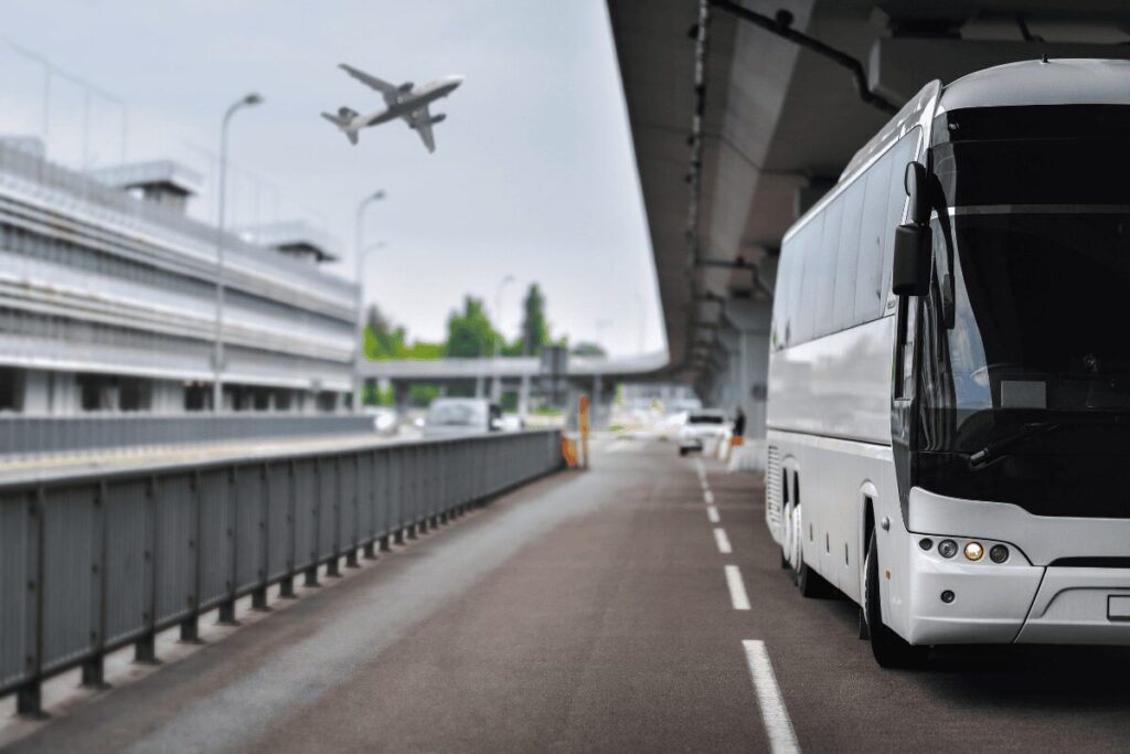 White Airport Express bus parked outside Prague Airport with a plane visible in the sky above